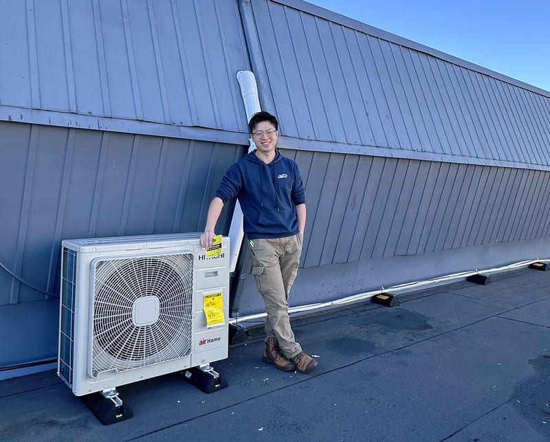 Thomas Lee on a commercial rooftop beside a ductless heat pump outdoor unit